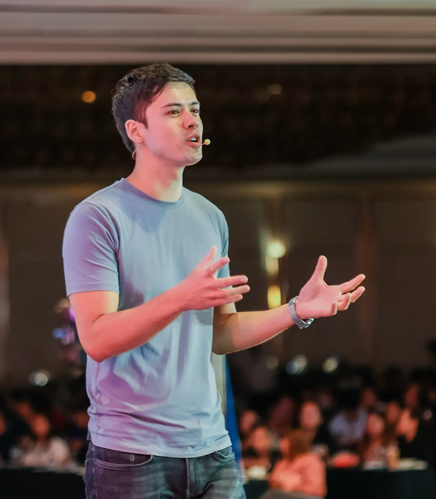 Mike Dee speaking on stage in a blue t-shirt